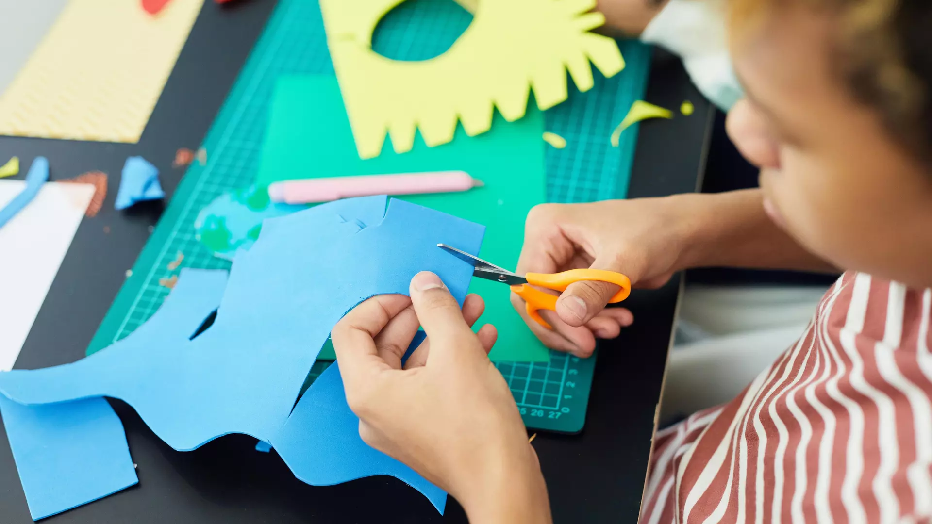 Kind schneidet aus Buntpapier aus.